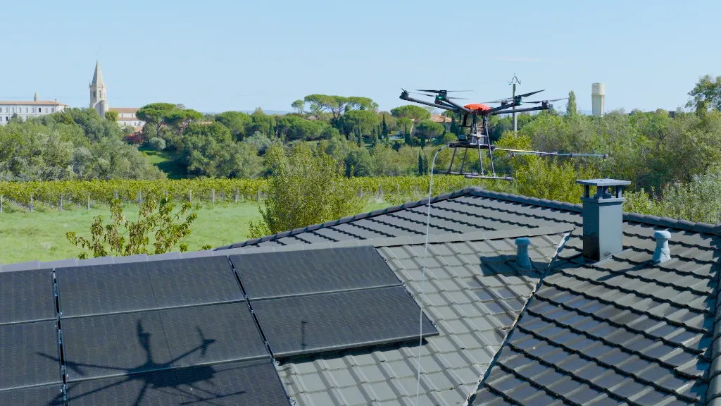 Drone professionnel pulvérisant près de panneaux photovoltaïques sur toiture — services techniques par drone : inspection, thermographie, photogrammétrie et nettoyage